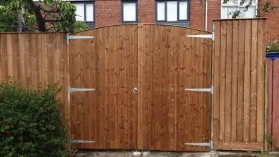 Tongue and groove arched wooden garden gates installed on a driveway, made from pressure-treated timber with ledge and brace design.